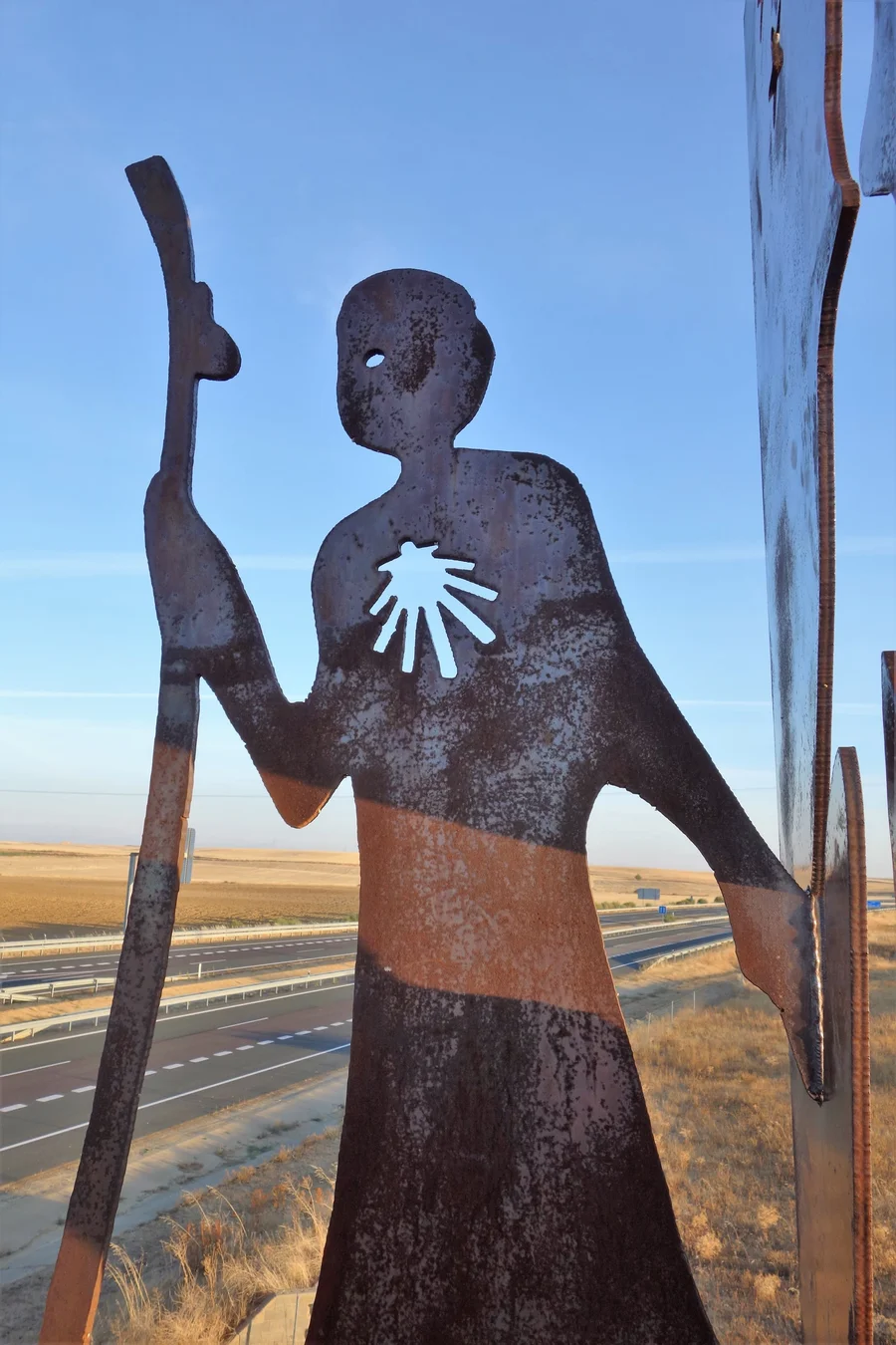 Eiserne Pilgerfigur mit Jakobsmuschel als Wegzeichen vor weitem Himmel